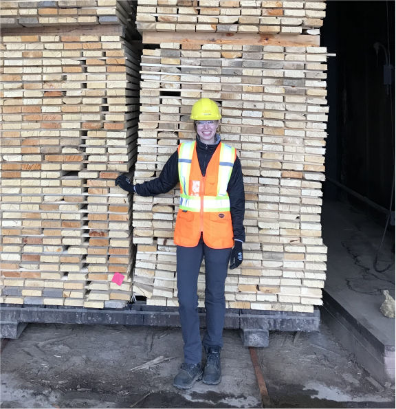 Alexa Gilbert standing in front of a lumber charge in a dry kiln